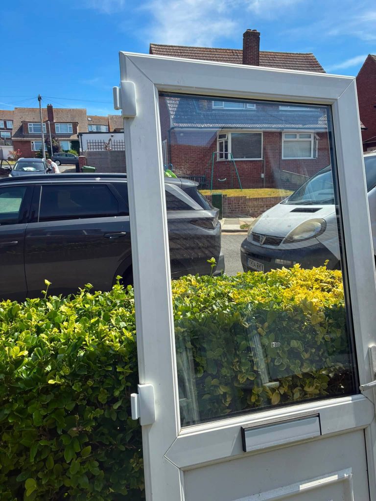 Upper half of a white UPVC door removed and resting outside during a hinge repair job by LBP Locksmiths in Portslade.